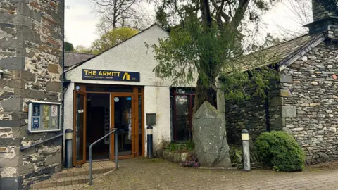 The Armitt The Armitt Library and Museum. The building is made of stone and is in keeping with the rural buildings found in the lake district. A tree has grown next to the entrance.