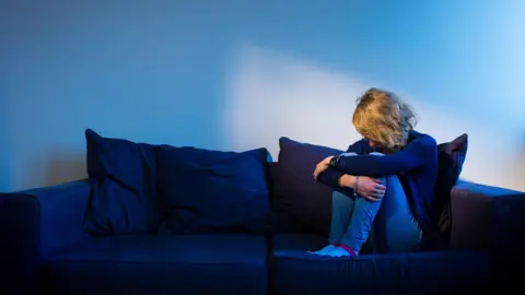 PA Media Sad person on sofa