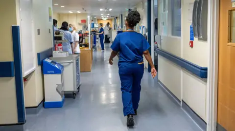 An NHS worker in blue scrubs walks through a hospital corridor