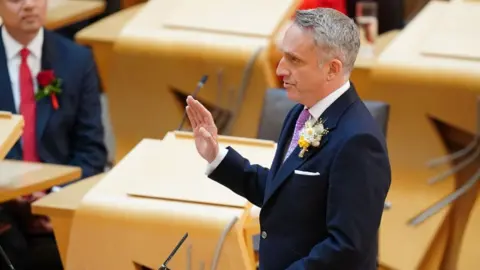 PA Media A man with grey hair with his hand raised 