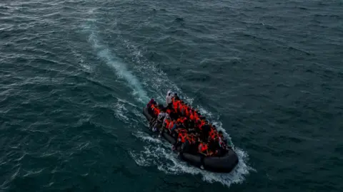 Reuters A dinghy pictured from above by a drone. The small boat is filled with figures wearing fluorescent life jackets