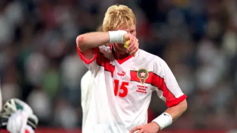 Getty Images Colin Hendry wipes a hand across his face as he stands in the football stadium in the red, green and white colours of Morocco.