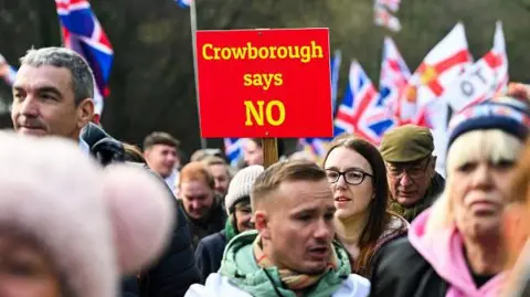 Getty Images People take part in a demonstration in Crowborough. A red sign reading "Crowborough says NO" is held above the crowd, with Union flags visible behind it.