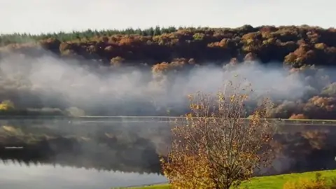 Trimpley Reservoir has a layer of mist hanging over its surface, in an autumnal scene with trees on either side reflecting colours of the season