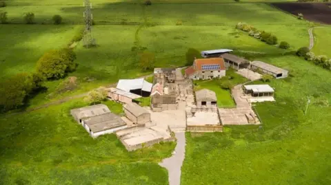 An aerial image of the existing farm buildings at Honeygar Farm. It shows lots of barns and outhouses in the middle of bright green fields.