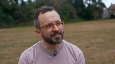 Hannah Roe/BBC Ben Conway pictured at the green space on Riddles Road in Sittingbourne. He is wearing orange framed glasses and a purple t-shirt.