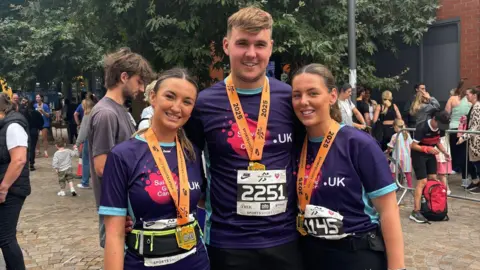 Shannon Griffiths three people stand in medals and purple charity t shirts they are wearing running gear.