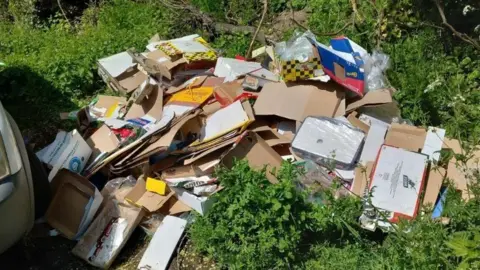 Cardboard boxes are dumped on grass.