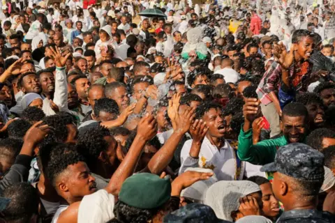 EPA A large crowd of worshippers hold their hands up as they are being sprayed with water in a symbolic baptism. 