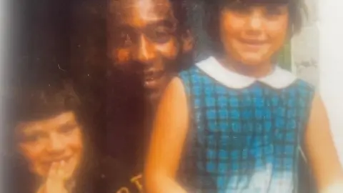 Laurence Bennett Laurence Bennett is sitting next to Pele and smiling with his hands close to his mouth. A girl is standing on the other side of Pele.