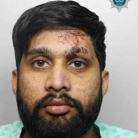 Staffordshire Police A mugshot of a man with black hair and a black beard. He is wearing a light green-coloured shirt.