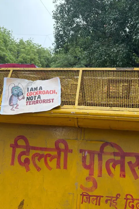 Geeta Pandey/BBC A Delhi police barricade with a poster that says "I am a cockroach, not a terrorist"