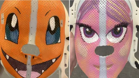 CUH Two radiotherapy masks. The one on the left is a Pokémon character which is orange and has large eyes. The one on the right is a pink and purple unicorn.