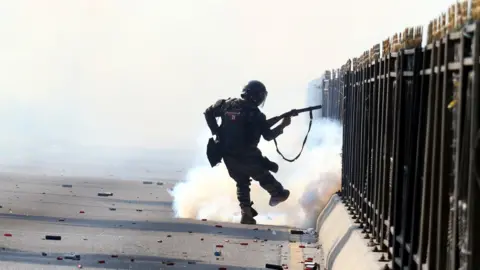 EPA A soldier appears to fire tear gas on a street littered with cartridges. He is silhouetted against the smoke