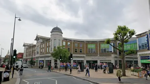 A Google image of Wimbledon Broadway - there are people shopping and cars driving along the road. 