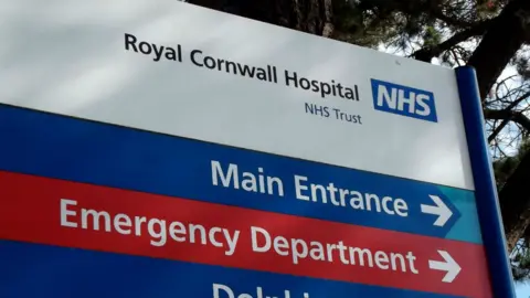 A sign at the Royal Cornwall Hospital in blue, white and red. It features the names of areas and indication arrows, including "Main Entrance" and "Emergency Department"