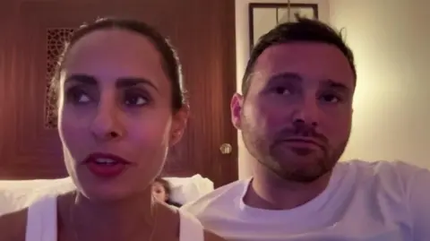 Layla Hamood and her husband Matty McGinn, both wearing white T-shirts speak to the BBC from their hotel bedroom