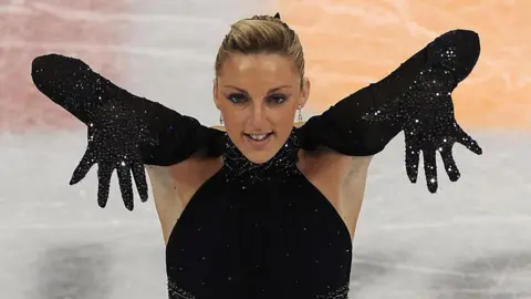 Getty Images Jenna McCorkell has her blonde hair in a bun. She is wearing a black sequined top and long gloves. 