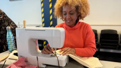 A women wearing an orange jumper using a white sewing machine