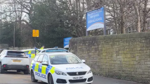 Tom Ingall/BBC A police car outside a tall stone wall which has a sign for the school on top.