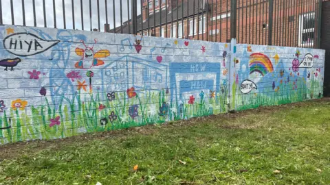 Bright, blue wall artistic wall with graffiti of rainbows, buildings, green grass and butterflies