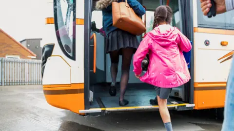 Getty Images Two girls getting on board an orange school bus