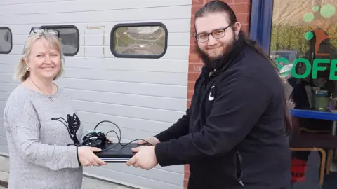 Reilly Allen, Community Larder Assistant at SOFEA handing a laptop to Jane Tyndall, Development Officer at Cholsey Volunteers