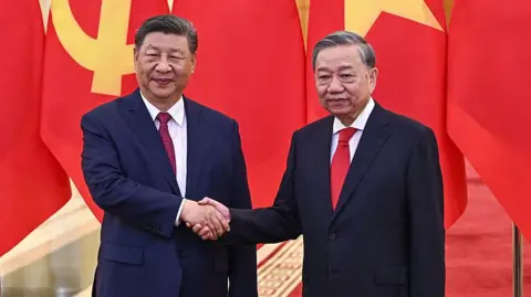 Getty Images Chinese president Xi Jinping shakes hands with Tô Lâm as both stand in front of large China flags. Both men are wearing suits