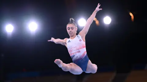 Reuters Jessica Gadirova jumps in the air with her legs straight and arms outstretched. She is wearing a Team GB leotard and her brown hair is in a tight bun on the top of her head. 