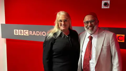 Selina Sasse Selina Sasse and Imam Monawar Hussain smiling for the camera at BBC Oxford's radio studio. The logo is on the wall behind them.