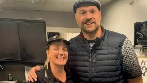 TERRY's TATO's LTD Rachel wears he Terry's Tato's uniform and stands next to Tyson who wears a farmer's cap and puffer gilet, they both smile brightly.