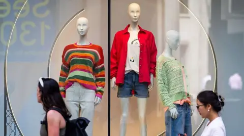 Getty Images Two women walking past a clothes shop that has three mannequins dressed in brightly coloured clothes