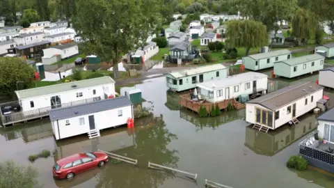 PA Media White mobile homes surrounded by water.  A red car is also visible.