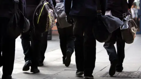 PA Media A group in school uniform, carrying bags, are walking away from the camera. None of them can be identified.