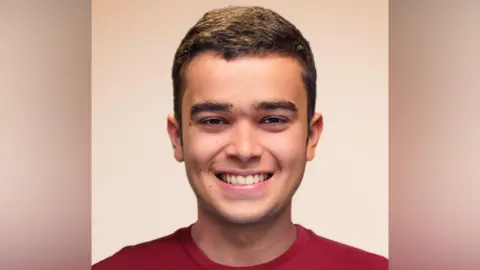 Opus Dei Pedro Ballester has brown cropped hair. He wears a red T-shirt and is smiling into the camera.