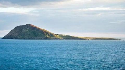 An island surrounded by a blue sea and grey skies