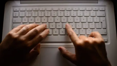 A close-up of hands typing on a white computer keyboard.