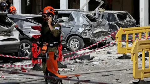 A rescuer uses his phone at an impact site following a missile strike from Iran on Israel, in Holon, Israel June 19, 2025. REUTERS/Violeta Santos Moura