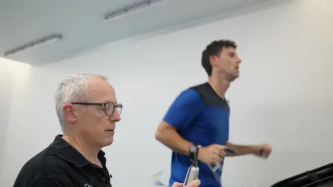 A man holding a probe, while another man runs in the background.
