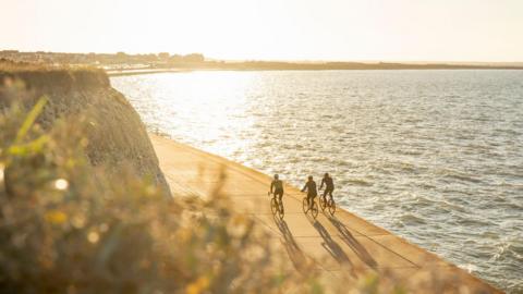Three cyclists on a coastal path in Kent at sunset with the sea in the background