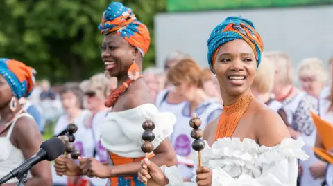 James Bass Photography Two women with blue and orange headdresses, white tops and orange necklaces
