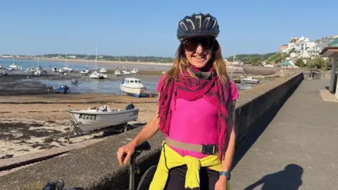 Debbie Krupski pictured in Gorey harbour. She is wearing a pink T-shirt and a pink scarf. She has a cycle helmet on and is pictured with her bike. 