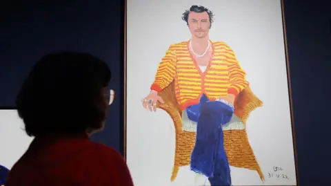 EPA A person looks at a painting of Harry Styles, who sits in a red and yellow striped jumper and blue jeans