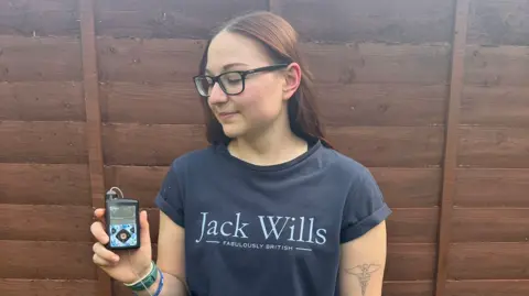Chloe Hammond A woman in a blue Jack Wills T-shirt looks down at a pump device she is holding in her right hand.