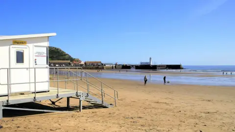 View of Bridlington's South beach - there is a lifeguard station in the foreground with people seen walking a dog on the beach close to the sea.