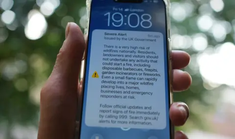 PA A hand holds a mobile phone displaying the government wildfire alert on the screen