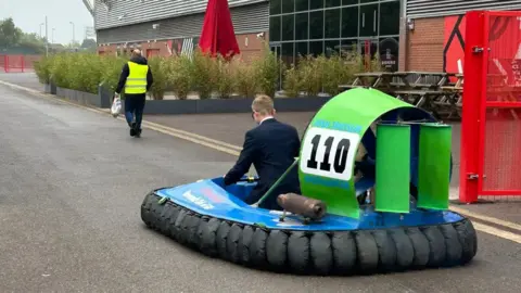 Family handout A photo taken from behind showing a young teenage boy driving a blue and green hovercraft with a red brick building in the background