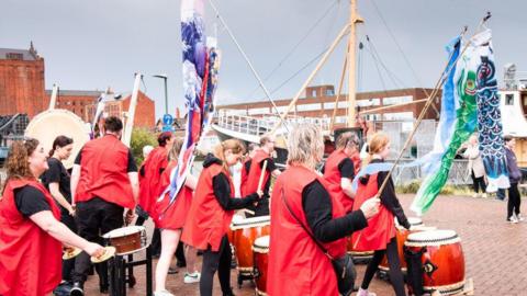 A band march with drums close to a ship