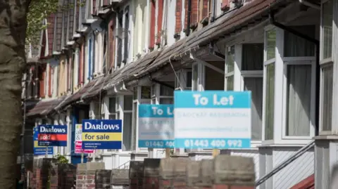 Getty Images The photo shows a row of houses with bay windows and different colour bricks. Most have a to let or for sale sign showing. The front sign is slightly blurred with the signs further down the street more in focus.