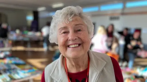 BBC Joyce Whitt smiling, with a room full of toys in the background